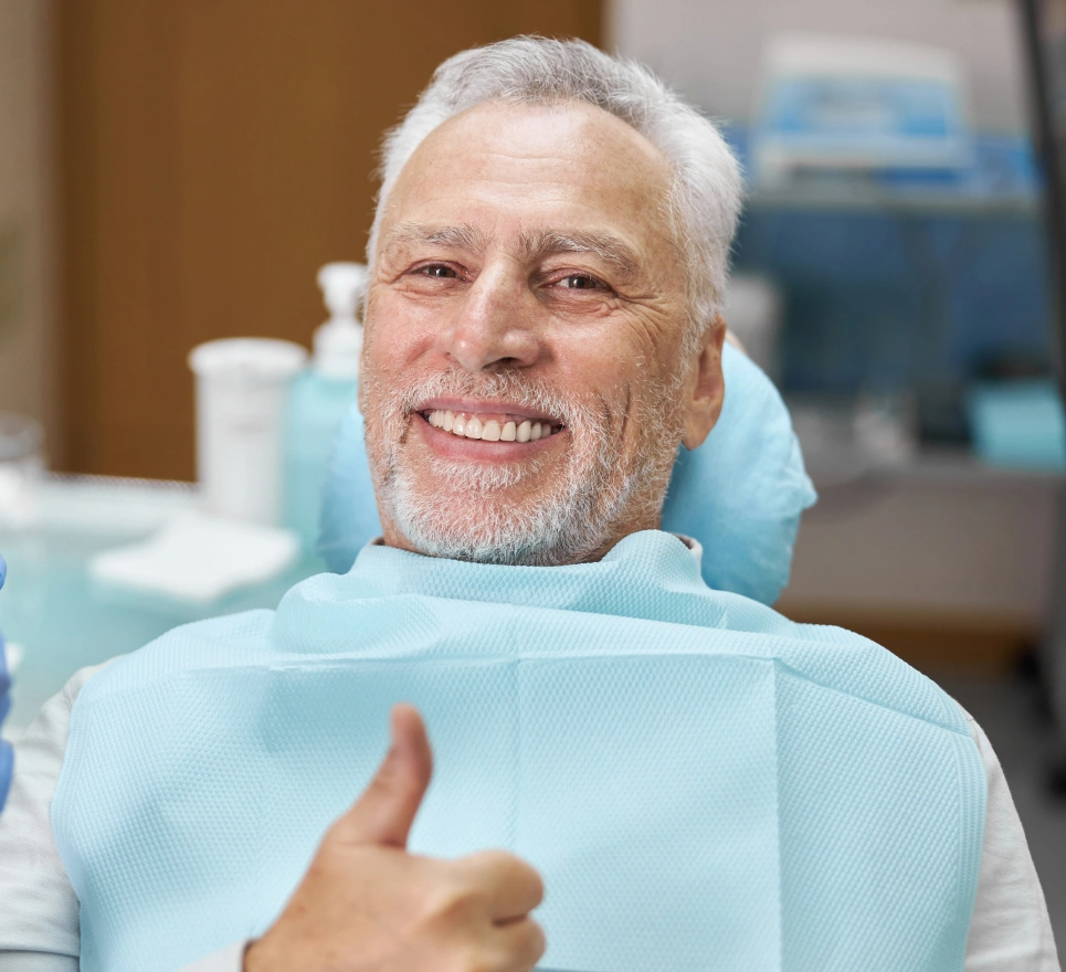 Senior man giving thumbs up in dental chair wearing bib at dental office