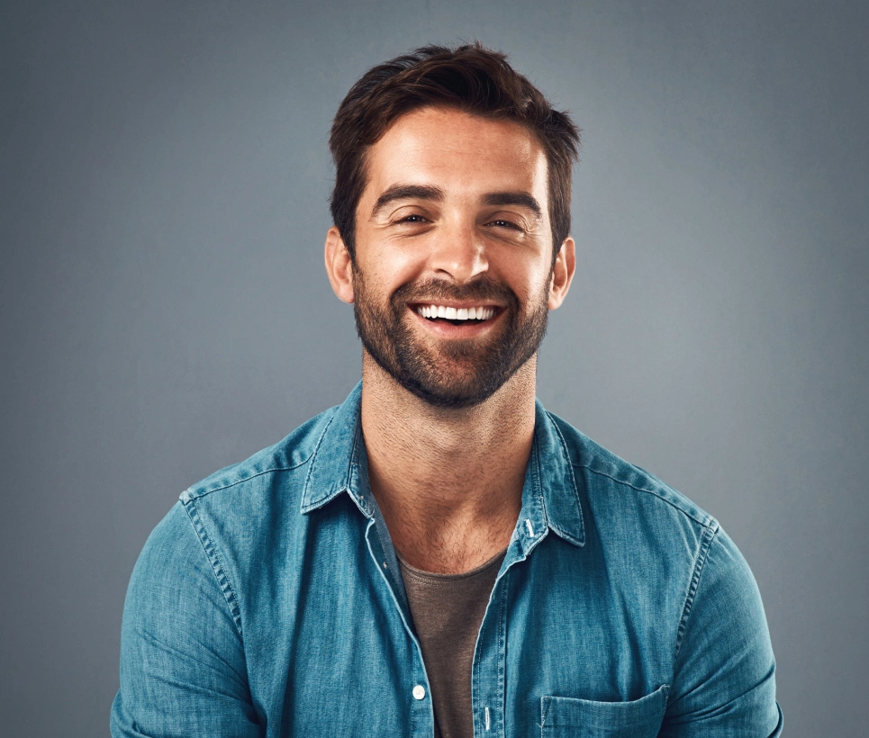 Smiling man in denim shirt against gray background, professional headshot for dental practice.