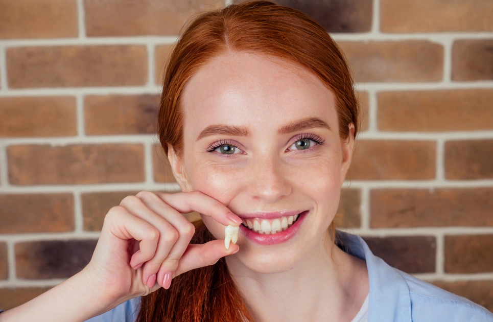 Young woman with red hair smiling while flossing teeth against brick wall background.