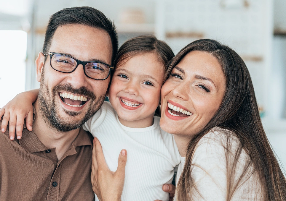 Happy family of three smiling together indoors in casual clothing.