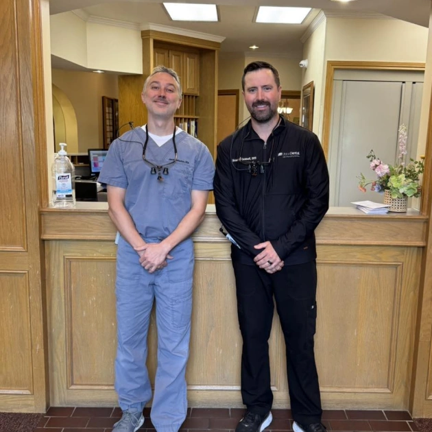 Two dental professionals in scrubs standing together in a modern dental office reception area.
