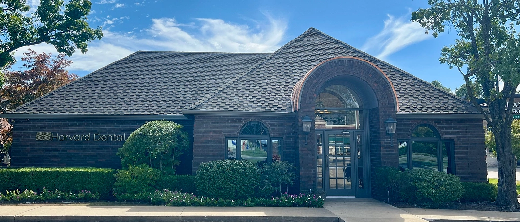Brick dental office building with arched entrance and manicured landscaping under blue sky.